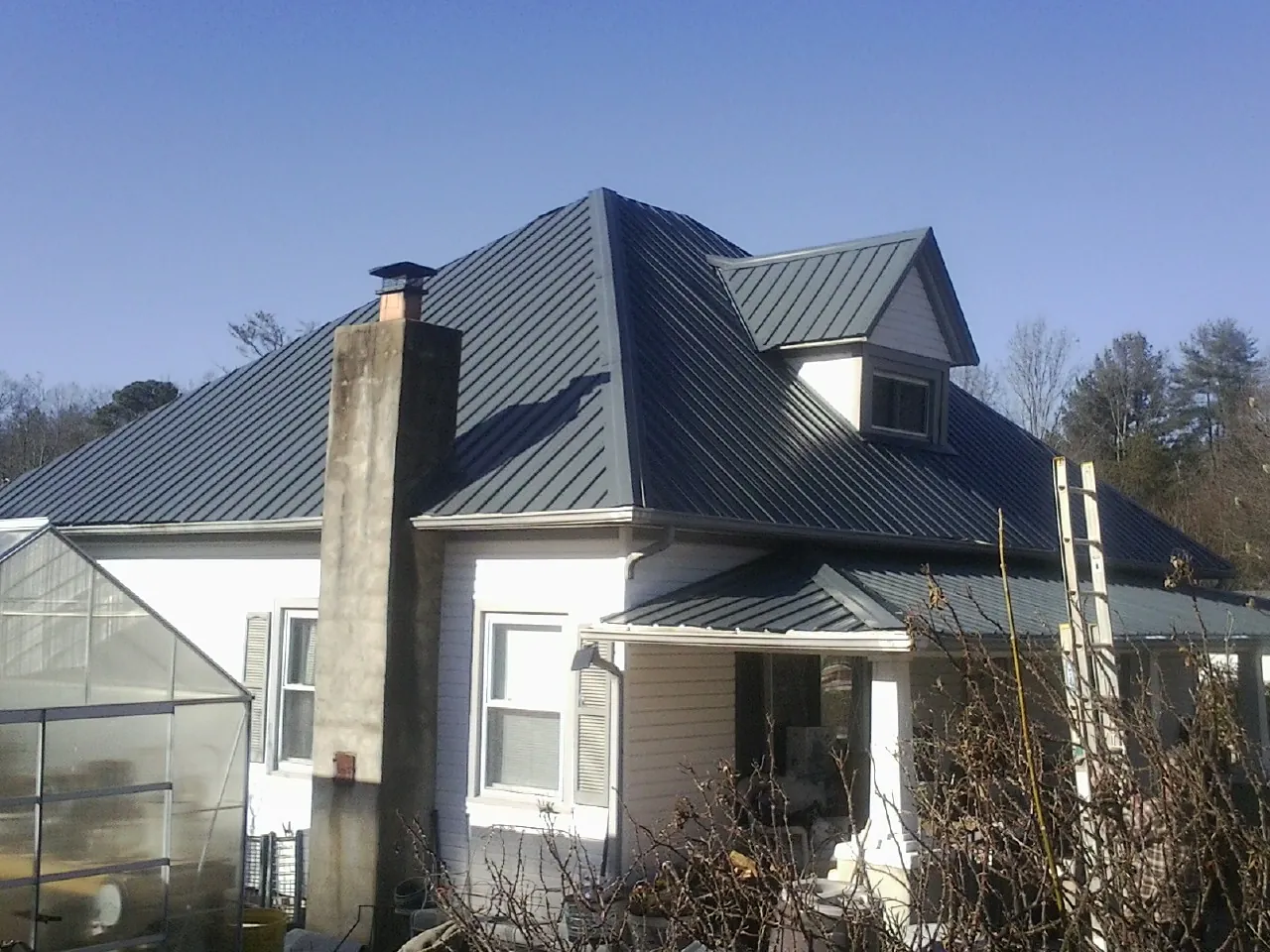 Dark blue standing seam metal roof on a white farmhouse with dormer — Slate & Tile Roof Repair by Roofing Brothers in Seeley Lake