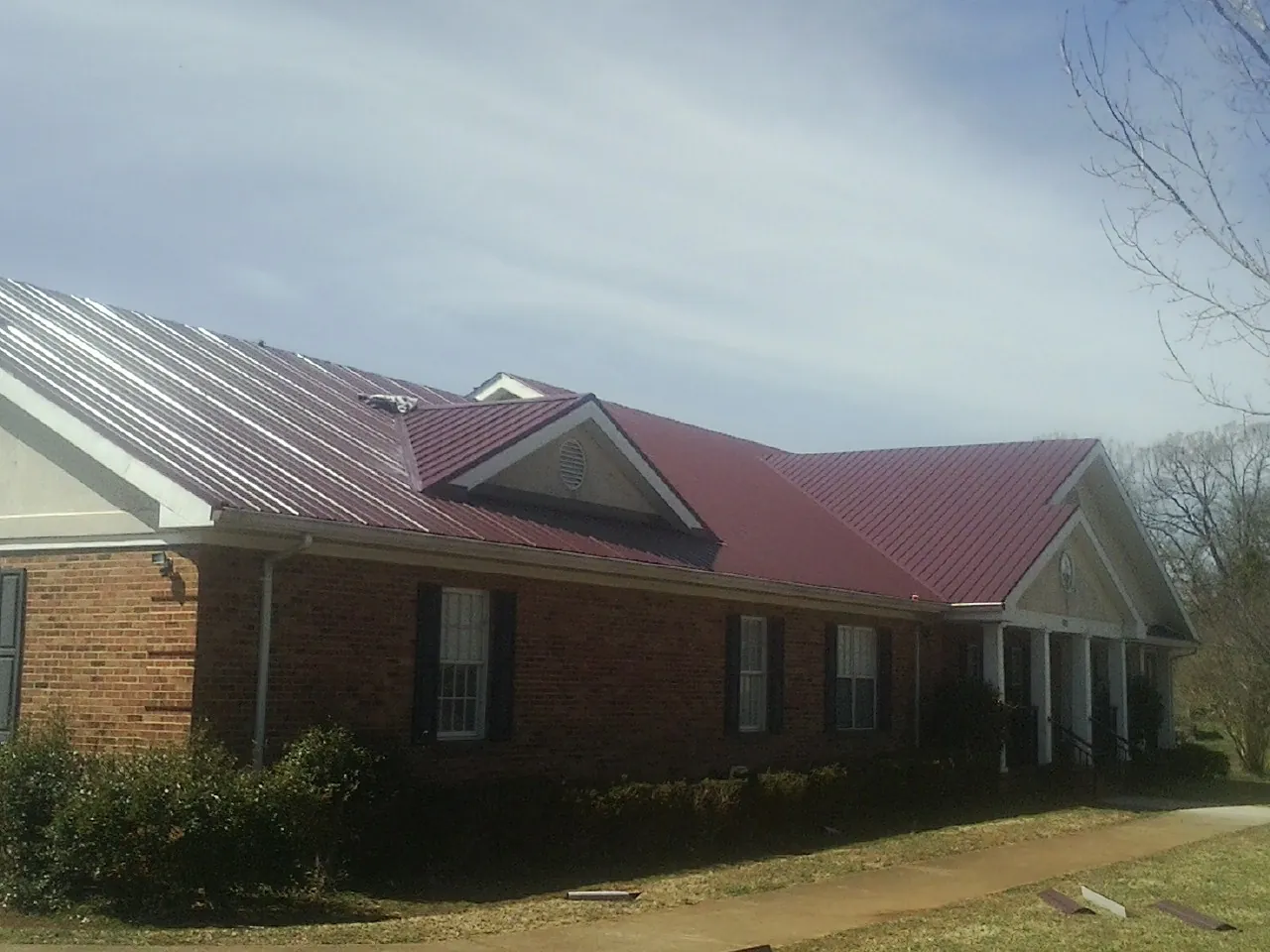 Red metal roof with gabled entries on a long brick building, from a Hail Damage Roof Repair job in Seeley Lake
