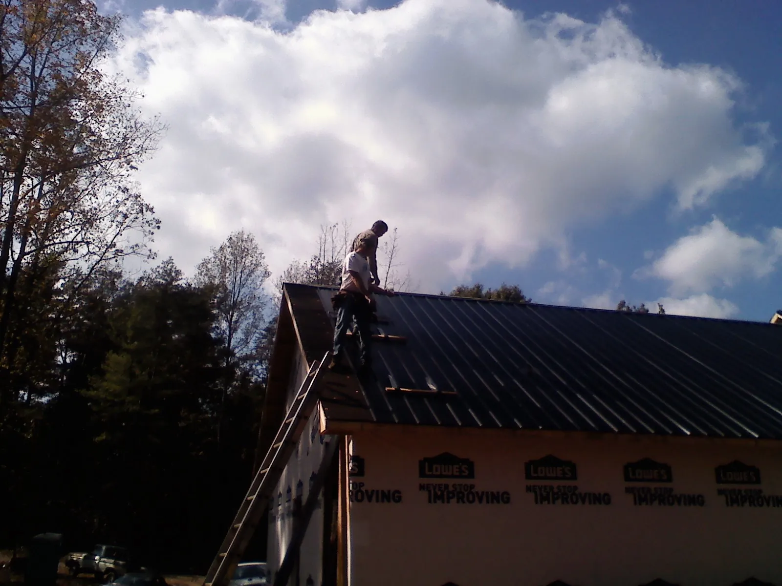 Roofer fastening dark metal panels high against a cloudy sky, from a Roof Inspection job in Seeley Lake