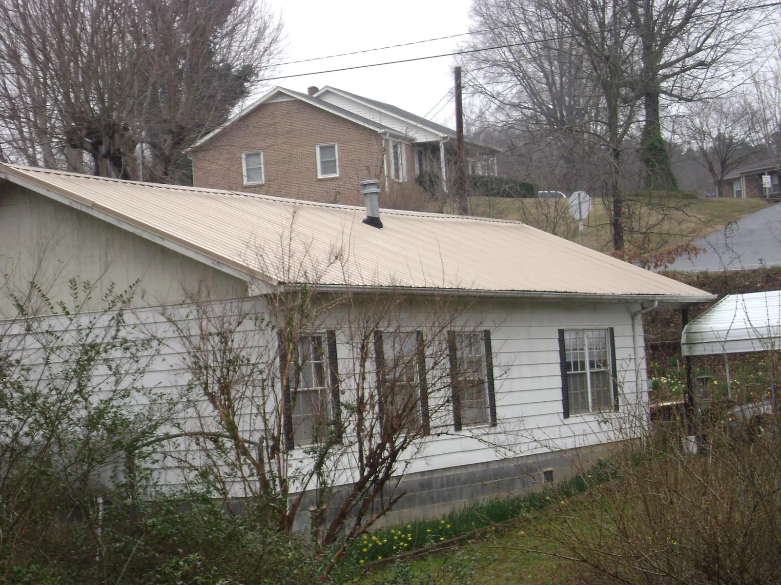 Tan metal roof on a white sided house set into a hillside — Commercial Roofing by Roofing Brothers in Seeley Lake